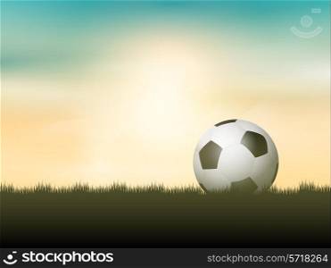 Soccer ball or football nestled in grass against a sunset sky