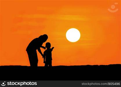 The silhouette of mother and son standing on the mountain watching the sunset.