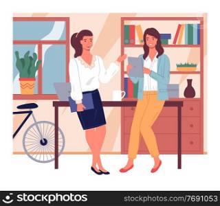 Two businesswomen talking lean at table. Young girl with digital tablet listening colleague with folder. Pretty women discussing work moments. Stylish interior with cabinet, bicycle at background. Businesswomen talking lean at table, young girl with digital tablet listening colleague with folder