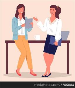Two modern women, office workers, clerks or colleagues communicate, leaning on the table. Woman with tablet in her hand, girl with folder in her hand. Laptop and cup on the table. Coffee break. Two women chatting in the office during a coffee break. Office staff, colleagues, employees