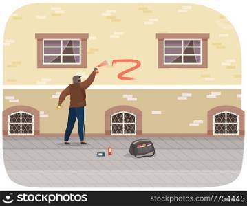 Vandal damaging city building. Bully in hood and balaclava painting graffiti on a brick wall of a residential building. Street gangsters and vandalism concept. A man bandit destroy city property. Vandal damaging city building. Bully in hood and balaclava painting graffiti on a brick wall