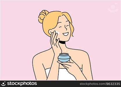 Woman applies anti-aging cream to face to stay beautiful, standing in bath towel after shower. Happy blonde girl smiles and uses cosmetic cream to help prevent wrinkles and pimples.. Woman applies anti-aging cream to face to stay beautiful, standing in bath towel after shower.