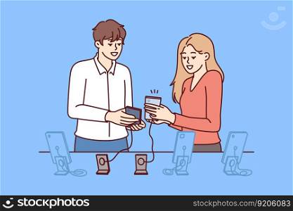 Woman buys new mobile phone in consultation with employee of digital gadget store. Man and girl are standing near showcase with smartphones connected by wire to counter, to avoid stealing phone . Woman buys new mobile phone in consultation with employee of digital gadget store
