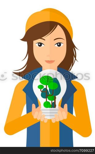 Woman holding in hands a big lightbulb with trees inside vector flat design illustration isolated on white background. Vertical layout.. Woman with lightbulb and trees inside.