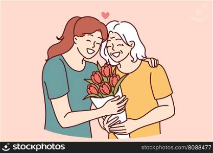 Woman hugs elderly mother and gives bouquet of flowers congratulating with birthday or mother day and thanks for good upbringing. Grown up daughter takes care of mother of retirement age . Woman hugs elderly mother and gives bouquet of flowers congratulating with birthday or mother day 