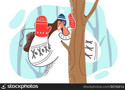 Woman in Scandinavian sweater waves hand standing in forest among trees during winter trip. Girl says hello raising hand with glove enjoying walk in winter park on Christmas weekend . Woman in Scandinavian sweater waves hand standing in forest among trees during winter trip