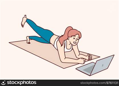 Woman is doing fitness lying on yoga mat and looking at laptop, listening to advice online trainer. Concept video lessons and distance training for athletes who want to do fitness without leaving home. Woman is doing fitness lying on yoga mat and looking at laptop, listening to advice online trainer