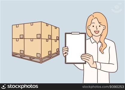 Woman logistician stands near boxes placed on pallet and demonstrates empty clipboard, advertising services of transport company. Girl logistician or storekeeper offers to use delivery services. Woman logistician stands near boxes placed on pallet and demonstrates empty clipboard