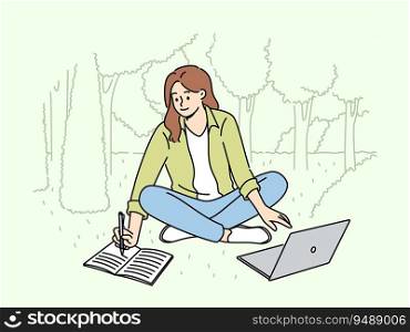 Woman student is sitting on lawn making notes in notebook and using laptop enjoying working in park. Happy girl student watching educational video and writing notes located in park. Woman student is sitting on lawn making notes in notebook and using laptop enjoying working in park