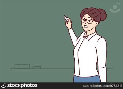 Woman teacher stands at blackboard and uses chalk, teaching elementary or high school children and giving students new knowledge. Happy teacher posing near empty chalkboard before class starts. Woman teacher stands at blackboard and uses chalk, teaching elementary or high school children