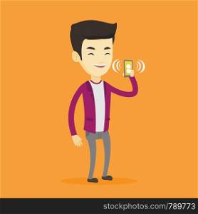 Young asian man holding ringing mobile phone. Smiling man answering a phone call. Man standing with ringing phone in hand. Vector flat design illustration isolated on blue background. Square layout.. Man holding ringing mobile phone.